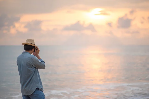 Young man traveler taking photos of sunset at tropical beach — Stock Photo, Image