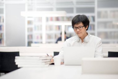 Genç Asyalı Üniversite öğrenci Kitaplığı'nda çalışma