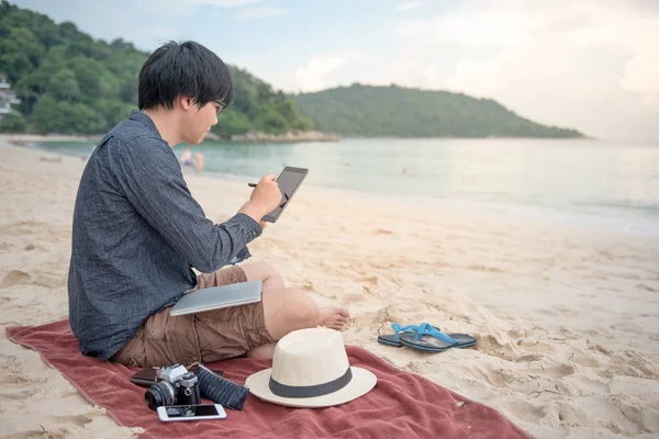 Jonge Aziatische man met behulp van de tablet op het strand — Stockfoto