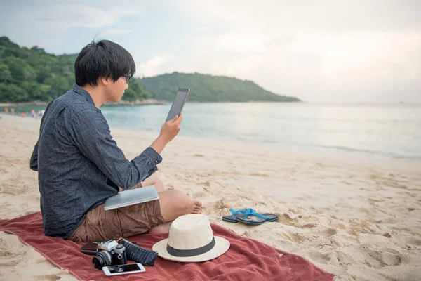 Jonge Aziatische man met behulp van de tablet op het strand — Stockfoto