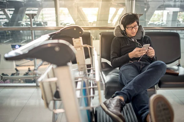 Joven asiático hombre escuchando música mientras espera en aeropuerto — Foto de Stock