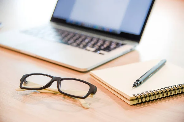 Glasses, notebook and laptop on wooden office desk