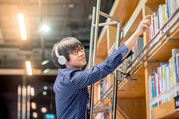 Joven asiático llegando a libro en la biblioteca — Foto de Stock