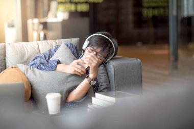 Genç Asyalı adam kanepede rahatlatıcı Smartphone kullanarak