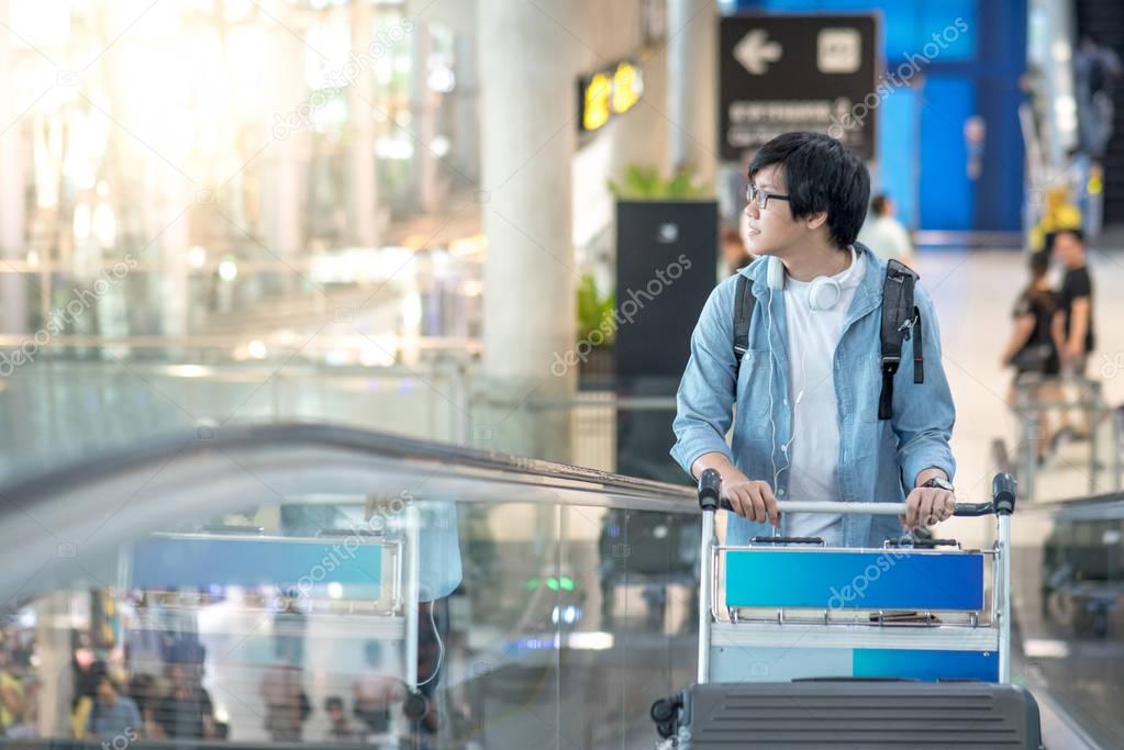 Young Asian man with airport trolley on escalator