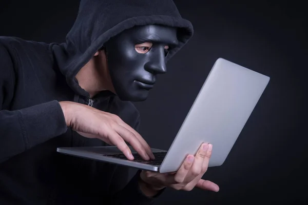Hacker maschio con maschera nera che trasporta laptop — Foto Stock
