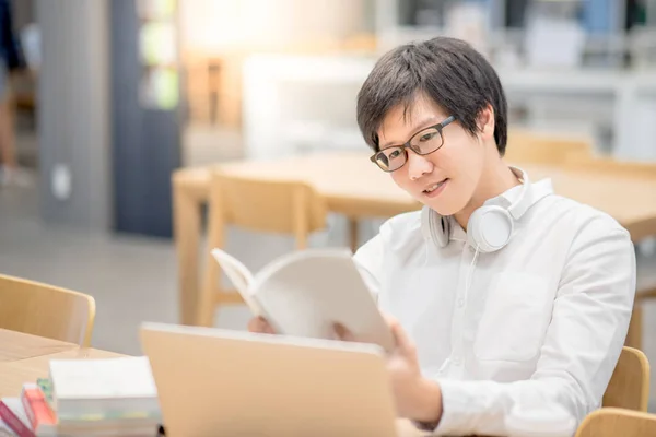 Young Asian man university student reading book in library