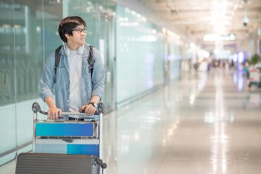 young asian man walking with trolley in airport terminal clipart