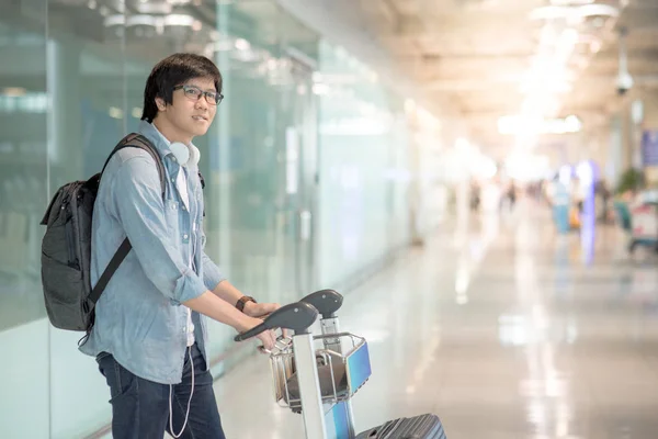 Joven asiático hombre caminando con carro en aeropuerto terminal — Foto de Stock