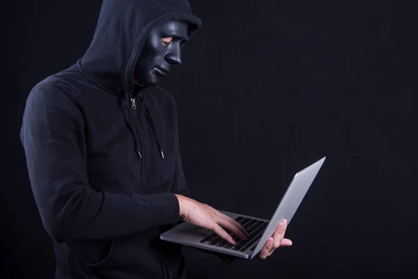 Hacker maschio con maschera nera che trasporta laptop — Foto Stock