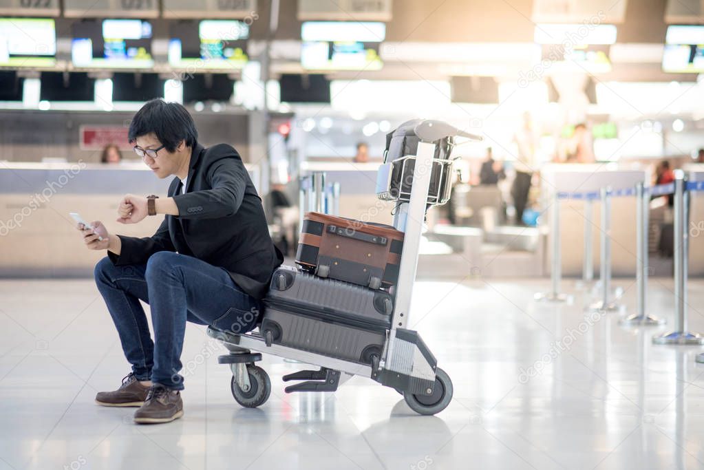Young Asian man sitting on trolley in airport terminal