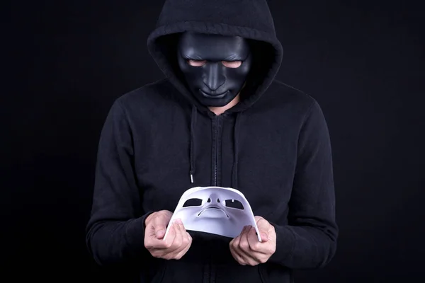 Mysteriöser Mann mit schwarzer Maske, der eine weiße Maske hält und auf sie blickt. Anonyme soziale Maskierung oder Halloween-Konzept. — Stockbild Mysteriöser Mann mit weißer Maske — Stockfoto