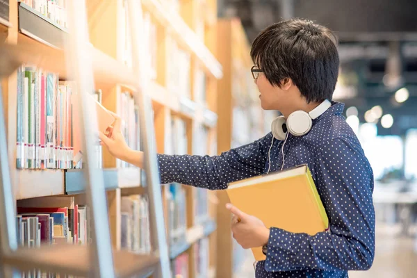 Joven asiático hombre estudiante elegir libro en biblioteca — Foto de Stock