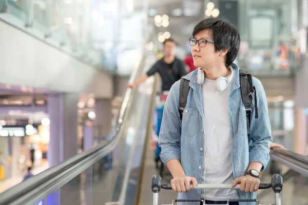 Joven asiático hombre con carro del aeropuerto en escaleras mecánicas — Foto de Stock