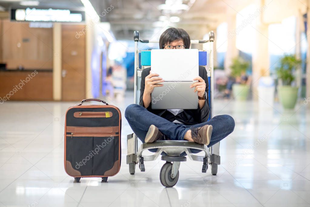 Young asian man holding laptop on airport trolley