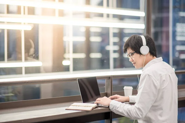 Joven asiático escuchando música mientras trabaja — Foto de Stock