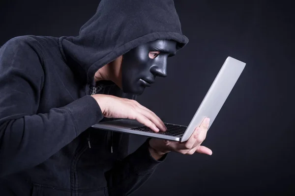 Mand hacker med sort maske transporterer laptop - Stock-foto