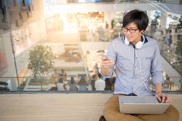 Jonge Aziatische man met smartphone en laptop — Stockfoto