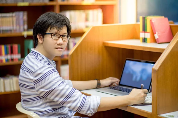 Jeune asiatique homme étudiant à l'université en utilisant un ordinateur portable dans la bibliothèque — Photo