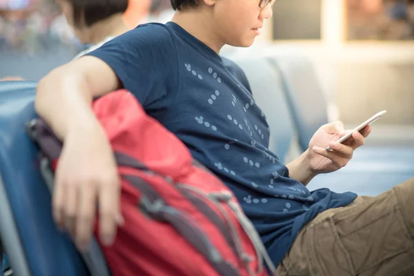 Nuori aasialainen mies käyttää älypuhelinta lentokentän terminaalissa — kuvapankkivalokuva