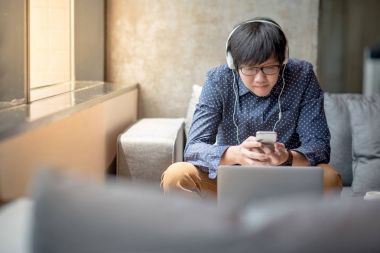 Genç Asyalı adam kanepede rahatlatıcı Smartphone kullanarak