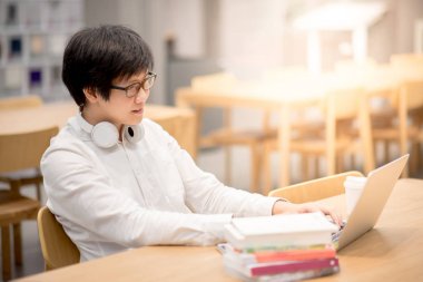 Genç Asyalı adam Üniversitesi Öğrenci Kitaplığı'nda çalışma