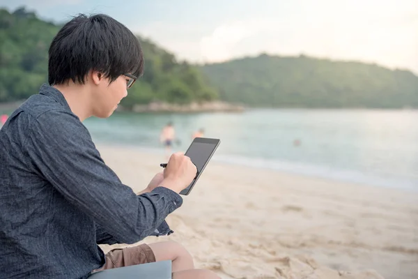 Jonge Aziatische man met behulp van de tablet op het strand — Stockfoto