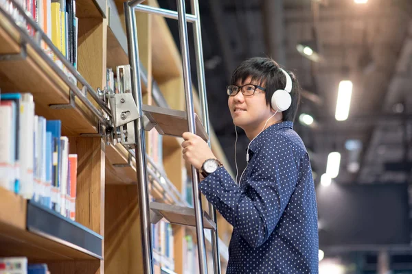 Jeune homme asiatique choisir un livre en utilisant l'échelle dans la bibliothèque — Photo