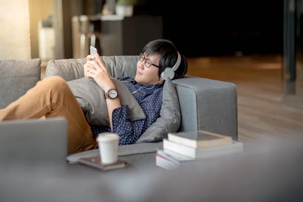 Jovem homem asiático usando smartphone relaxante no sofá — Fotografia de Stock