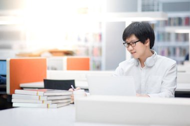 Genç Asyalı adam Üniversitesi Öğrenci Kitaplığı'nda çalışma