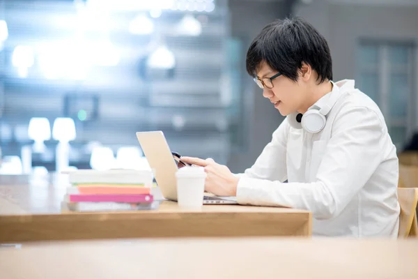 Jovem asiático estudante universitário usando smartphone na biblioteca — Fotografia de Stock