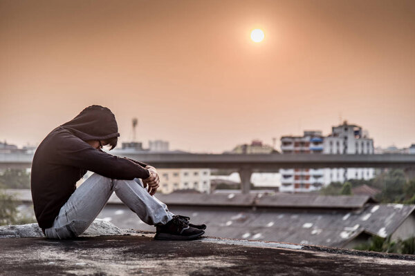 Young Asian man sitting rooftop of building with depression stre
