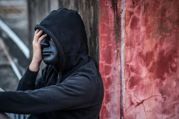 Tajemnica człowieka z czarna maska uczucie podkreślił, siedzi w abandone — Zdjęcie stockowe