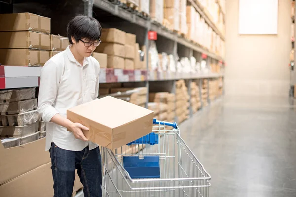 Ung asiatisk man sätta papper box i vagnens varukorg i lager — Stockfoto