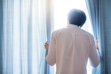 Genç Asyalı adam mavi perde oturma odasında açılış