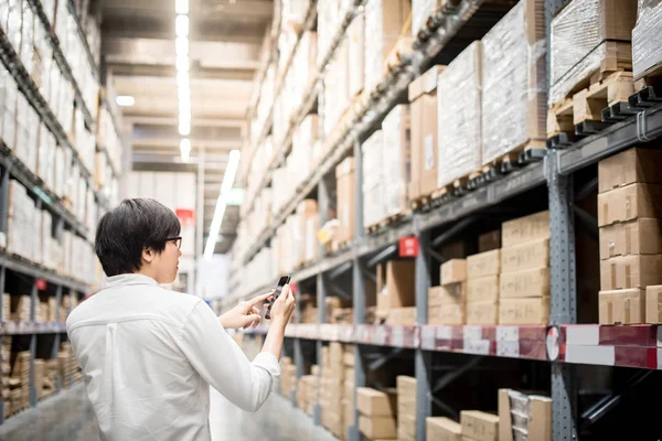 Joven asiático hombre comprobar la lista de compras desde el teléfono inteligente en wareho — Foto de Stock