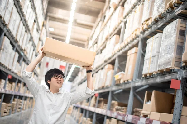 Joven asiático hombre llevar papel caja sobre cabeza en almacén — Foto de Stock