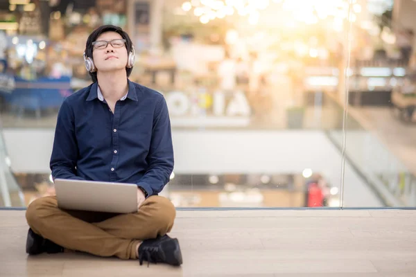 Jovem homem de negócios asiático ouvindo música enquanto usa laptop — Fotografia de Stock