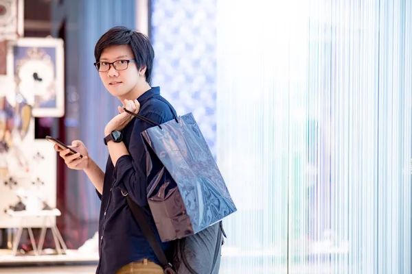 Young Asian man holding blue shopping bag in department store — Stock Photo, Image