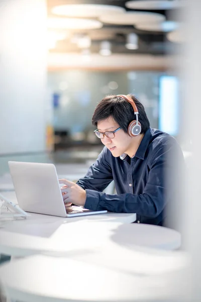 Jovem homem de negócios asiático ouvindo música enquanto trabalhava com l — Fotografia de Stock
