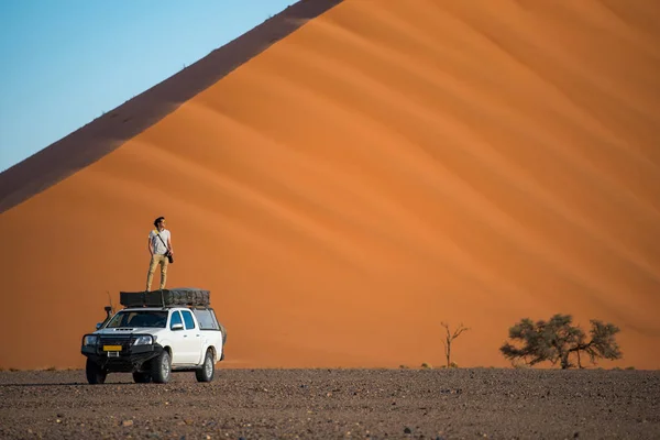 Junger asiatischer Mann steht auf Wohnmobil in der Nähe von orangefarbenem Sand — Stockfoto