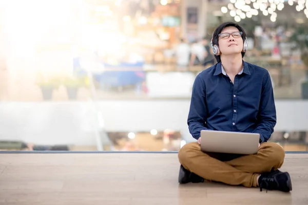 Jovem homem de negócios asiático ouvindo música enquanto usa laptop — Fotografia de Stock