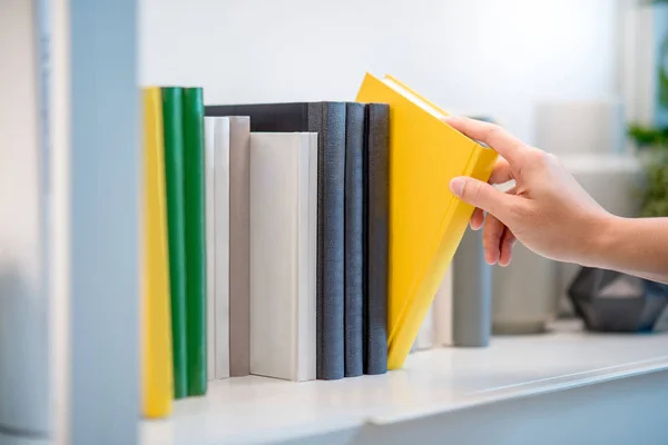 Male hand picking yellow book on white bookshelf