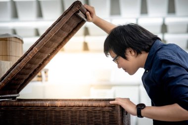 Genç Asyalı adam büyük bir dokuma ahşap kutu içinde seyir açma. Ev dekorasyon konsepti