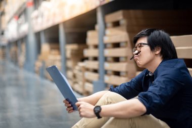 Genç Asyalı adam Stocktaking düşünme ürünün depoda raf karton kutu, kağıt ve pano kullanarak yapıyor. fiziksel envanter sayım kavramı