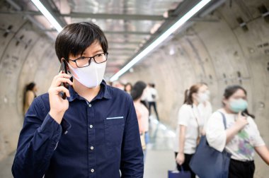 Asyalı adam metroda telefon kullanarak maske takıyor.