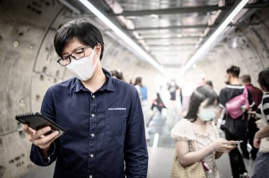 Asyalı adam metroda telefon kullanarak maske takıyor.