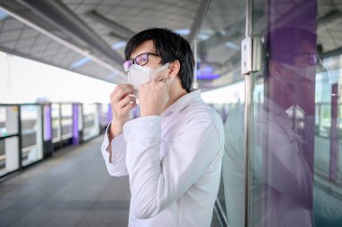Skytrain istasyonunda ya da tren istasyonunda yüz maskesi takan Asyalı bir adam. Wuhan Coronavirus (COVID-19) toplu taşımacılıkta salgın önleme. PM2.5 hava kirliliğine karşı sağlık bilinci.