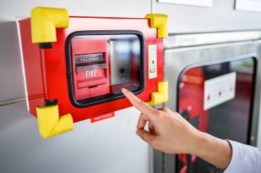 Ofis binasındaki beton duvardaki kırmızı yangın alarmına bakan erkek eli. Endüstriyel yangın alarmı sistemi acil durum ekipmanı.