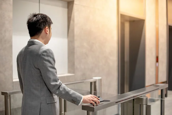 Asian businessman in formal business wear using smartphone to open automatic gate machine in office building. Working routine concept